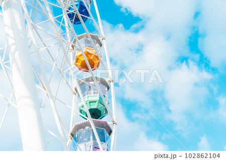 Bottom view of Ferris wheel part with multicolor cabins on the background of blue sky with clouds. Selective focus, copy space. 102862104