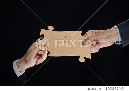 Close-up of business partners putting together white puzzle pieces on black background Close-up of business partners putting together white puzzle pieces on black background 102862144