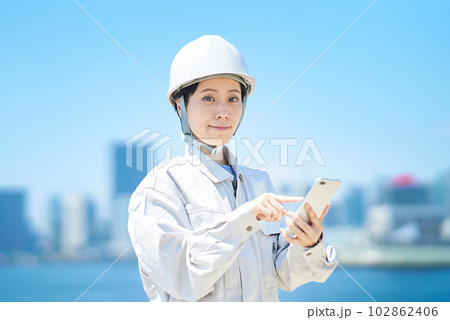 スマートフォンを手にする作業服姿の女性 スマートフォンを手にする作業服姿の女性 102862406