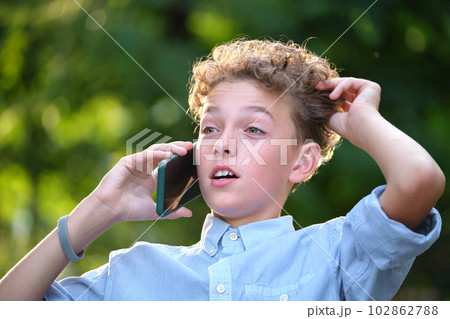 Young puzzled child boy talking on cellphone outdoors in summer park 102862788