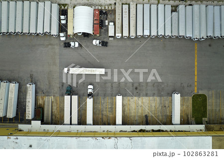 Top view of giant logistics center with many commercial trailer trucks unloading and uploading retail products for further shipment. Global economy concept Top view of giant logistics center with many commercial trailer trucks unloading and uploading retail products for further shipment. Global economy concept 102863281