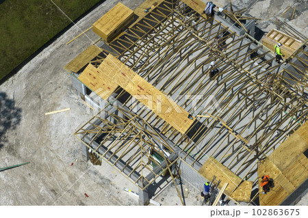 Professional builders working on roof construction of unfinished suburban home with wooden frame structure in Florida rural area. Concept of housing development in America Professional builders working on roof construction of unfinished suburban home with wooden frame structure in Florida rural area. Concept of housing development in America 102863675