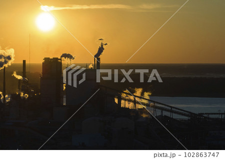 Huge factory with high chimneys polluting atmosphere with carbon dioxide smoke from production process at plant manufacturing yard. Industrial site at sunset Huge factory with high chimneys polluting atmosphere with carbon dioxide smoke from production process at plant manufacturing yard. Industrial site at sunset 102863747
