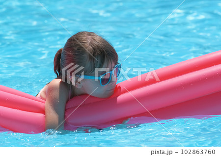 Happy child girl relaxing on inflatable air mattress in swimming pool on sunny summer day during tropical vacations. Summertime activities concept Happy child girl relaxing on inflatable air mattress in swimming pool on sunny summer day during tropical vacations. Summertime activities concept 102863760