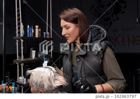 Brown-haired girl professional European hairdresser in the process of dyeing the client's head hair with a brush at work in a barbershop 102863797
