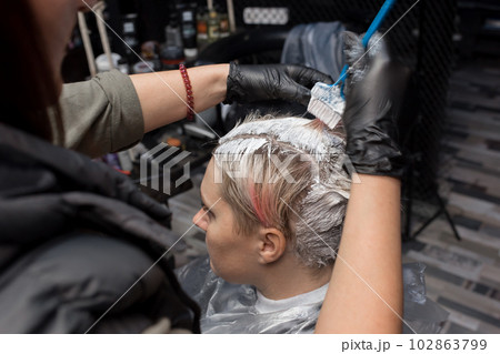 Close-up hairdresser's hands painting the client's head, hair, roots with a brush in a barbershop 102863799