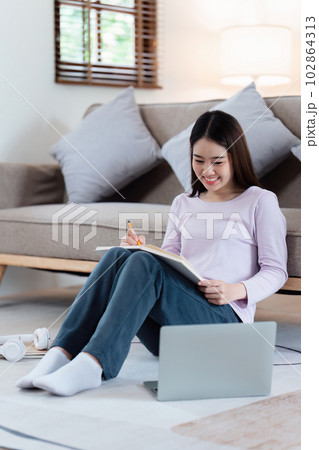 Online education, e-learning. Asian woman in stylish casual clothes, studying using a laptop, listening to online lecture, taking notes, online study at home 102864313