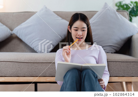 Online education, e-learning. Asian woman in stylish casual clothes, studying using a laptop, listening to online lecture, taking notes, online study at home Online education, e-learning. Asian woman in stylish casual clothes, studying using a laptop, listening to online lecture, taking notes, online study at home 102864314