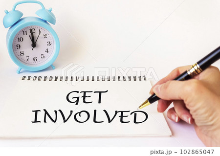 Text Get involved written on a notebook by a female hand, pen to the side on a white background Text Get involved written on a notebook by a female hand, pen to the side on a white background 102865047