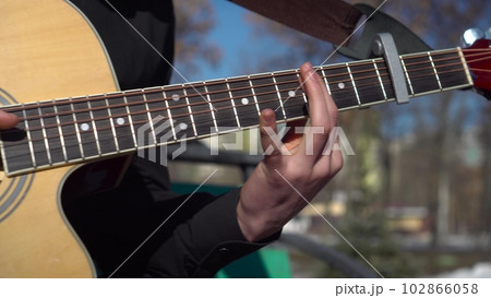 A young man plays the guitar in nature. The student masterfully plays the guitar and quickly plucks the strings. 102866058