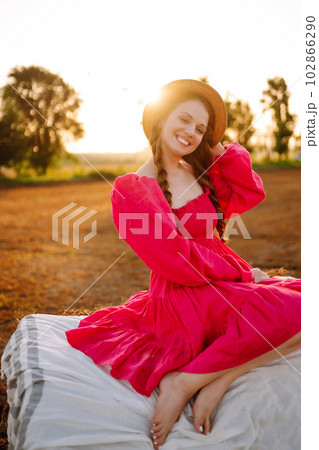 Beautiful curly woman in hat and clothes posing near hay bales in the countryside at sunset. Beautiful curly woman in hat and clothes posing near hay bales in the countryside at sunset. 102866290