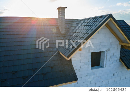 Aerial view of unfinished house with aerated lightweight concrete walls and wooden roof frame covered with metallic tiles under construction. 102866423