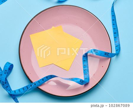 Round pink plate and centimeter on a blue background, weight loss concept Round pink plate and centimeter on a blue background, weight loss concept 102867089