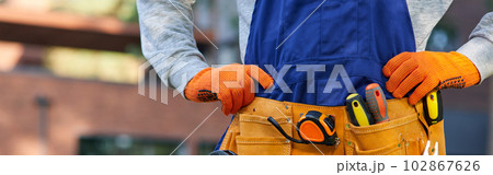 Male builder in blue overalls wearing tool belt. Close up on waist area Male builder in blue overalls wearing tool belt. Close up on waist area 102867626
