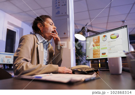 Tired corporate employee yawning in startup office after working overtime at financial strategy to help increase company profit. Exhausted overworked manager analyzing marketing graphs Tired corporate employee yawning in startup office after working overtime at financial strategy to help increase company profit. Exhausted overworked manager analyzing marketing graphs 102868314