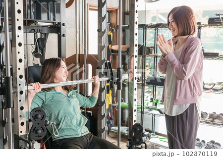 スポーツジムでマシンを使って筋トレするアジア人女性と応援する友人 102870119