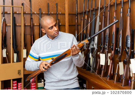 Focused Latino inspecting sporting shotgun in gunsmith shop 102870800