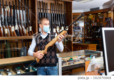 Gun store owner in medical mask offering break-barrel air rifle Gun store owner in medical mask offering break-barrel air rifle 102870868