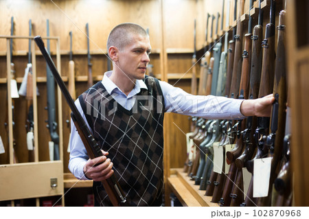 Man examining hunting shotgun before buying in gun store 102870968