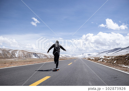 Asian woman skateboarder skateboarding on snowy country road 102873926