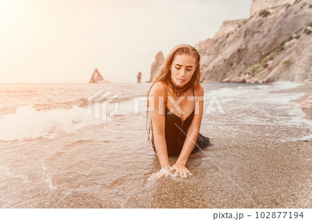 Woman summer travel sea. Happy tourist in black dress enjoy taking picture outdoors for memories. Woman traveler posing on sea beach surrounded by volcanic mountains, sharing travel adventure journey 102877194