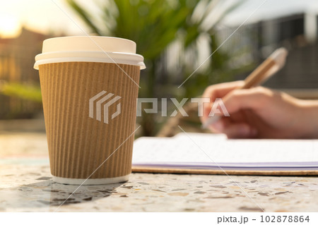 Unrecognizable Young woman study in beach resort. Drinking coffee from paper cup. Student making homework Female hands writing on notebook gratitude journal self reflection self discovery in Co 102878864