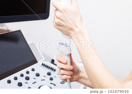 Woman doctor's hand applies a medical gel to ultrasonic sensor of ultrasound machine in the clinic. Woman doctor's hand applies a medical gel to ultrasonic sensor of ultrasound machine in the clinic. 102879030