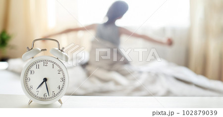 little boy sitting and stretching in bed at home in the morning with alarm clock 102879039