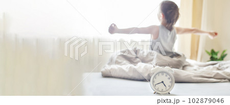 little boy sitting and stretching in bed at home in the morning with alarm clock little boy sitting and stretching in bed at home in the morning with alarm clock 102879046