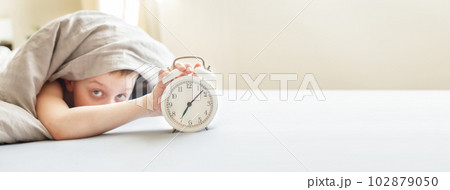boy lying on bed and stopping alarm clock in morning. childs hand reaching for alarm clock 102879050