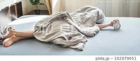 boy lying on bed and stopping alarm clock in morning. childs hand reaching for alarm clock boy lying on bed and stopping alarm clock in morning. childs hand reaching for alarm clock 102879051