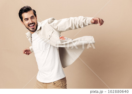 Stylish man smile runs and jumps on a beige background in a white t-shirt and business jacket, flying clothes hero, fashionable clothing style, copy space, space for text 102880640