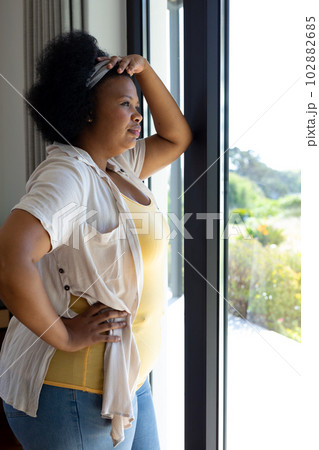 Thoughtful plus size african american woman leaning and looking out of window Thoughtful plus size african american woman leaning and looking out of window 102882685