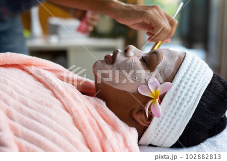 Relaxed plus size african american woman having beauty face mask applied to face at spa Relaxed plus size african american woman having beauty face mask applied to face at spa 102882813