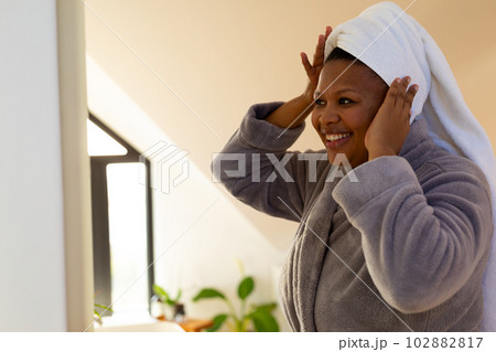Happy plus size african american woman wearing robe looking at herself in bathroom mirror Happy plus size african american woman wearing robe looking at herself in bathroom mirror 102882817