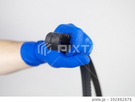 Timing belt cracked. Replacing a failed engine transmission belt. Cracks in rubber and risk of broken cords. Replacement of equipment according to the regulations. Mechanic in blue gloves 102882878