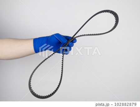 Timing belt cracked. Replacing a failed engine transmission belt. Cracks in rubber and risk of broken cords. Replacement of equipment according to the regulations. Mechanic in blue gloves 102882879