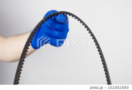 Timing belt cracked. Replacing a failed engine transmission belt. Cracks in rubber and risk of broken cords. Replacement of equipment according to the regulations. Mechanic in blue gloves 102882880