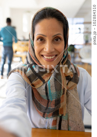 Portrait of happy muslim biracial businesswoman in headscarf looking at camera in modern office Portrait of happy muslim biracial businesswoman in headscarf looking at camera in modern office 102884310