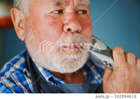 An elderly man trims his beard with an eclectic razor. ease of use of clippers. 102884618