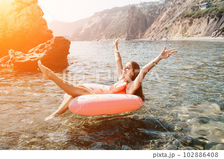 Woman summer sea. Happy woman swimming with inflatable donut on the beach in summer sunny day, surrounded by volcanic mountains. Summer vacation concept. 102886408