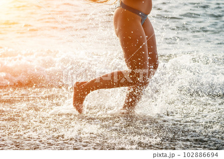 Running woman on a summer beach. A woman jogging on the beach at sunrise, with the soft light of the morning sun illuminating the sand and sea, evoking a sense of renewal, energy and health. 102886694