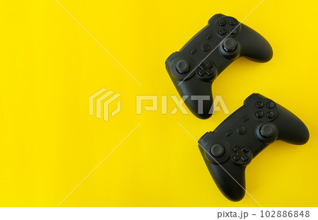 Isolated game joysticks on a yellow background. Gamer playing at home, relaxing with friends, competition. Isolated game joysticks on a yellow background. Gamer playing at home, relaxing with friends, competition. 102886848