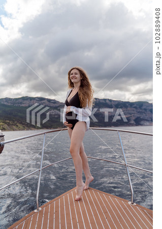 Woman on a yacht. Happy model in a swimsuit posing on a yacht against a blue sky with clouds and mountains 102889408