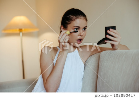 A woman at home looks in the mirror and apply makeup dye mascara eyelashes, beauty concept, care for problem skin with acne. 102890417