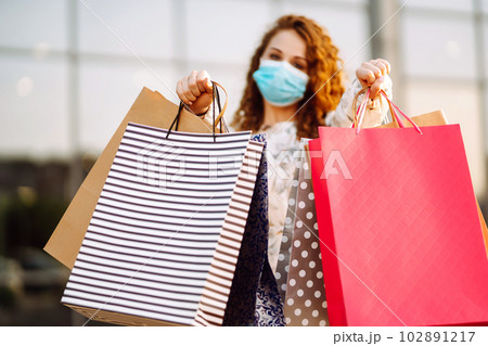 Woman in shopping. Young girl in protective sterile medical mask on her face with shopping bags. Woman in shopping. Young girl in protective sterile medical mask on her face with shopping bags. 102891217
