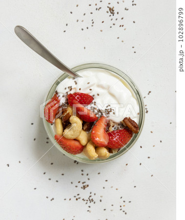 Greek yogurt, nuts and strawberries in a glass jar with a spoon on a white table top view Greek yogurt, nuts and strawberries in a glass jar with a spoon on a white table top view 102896799