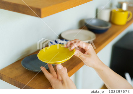 棚に食器を並べる女性の手元 102897678
