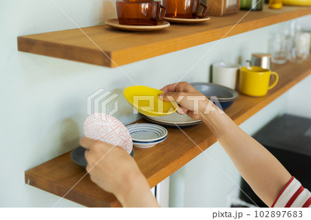 棚に食器を並べる女性の手元 102897683