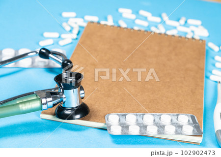 A medical notebook with a stethoscope and pills, a place for text, blue background A medical notebook with a stethoscope and pills, a place for text, blue background 102902473
